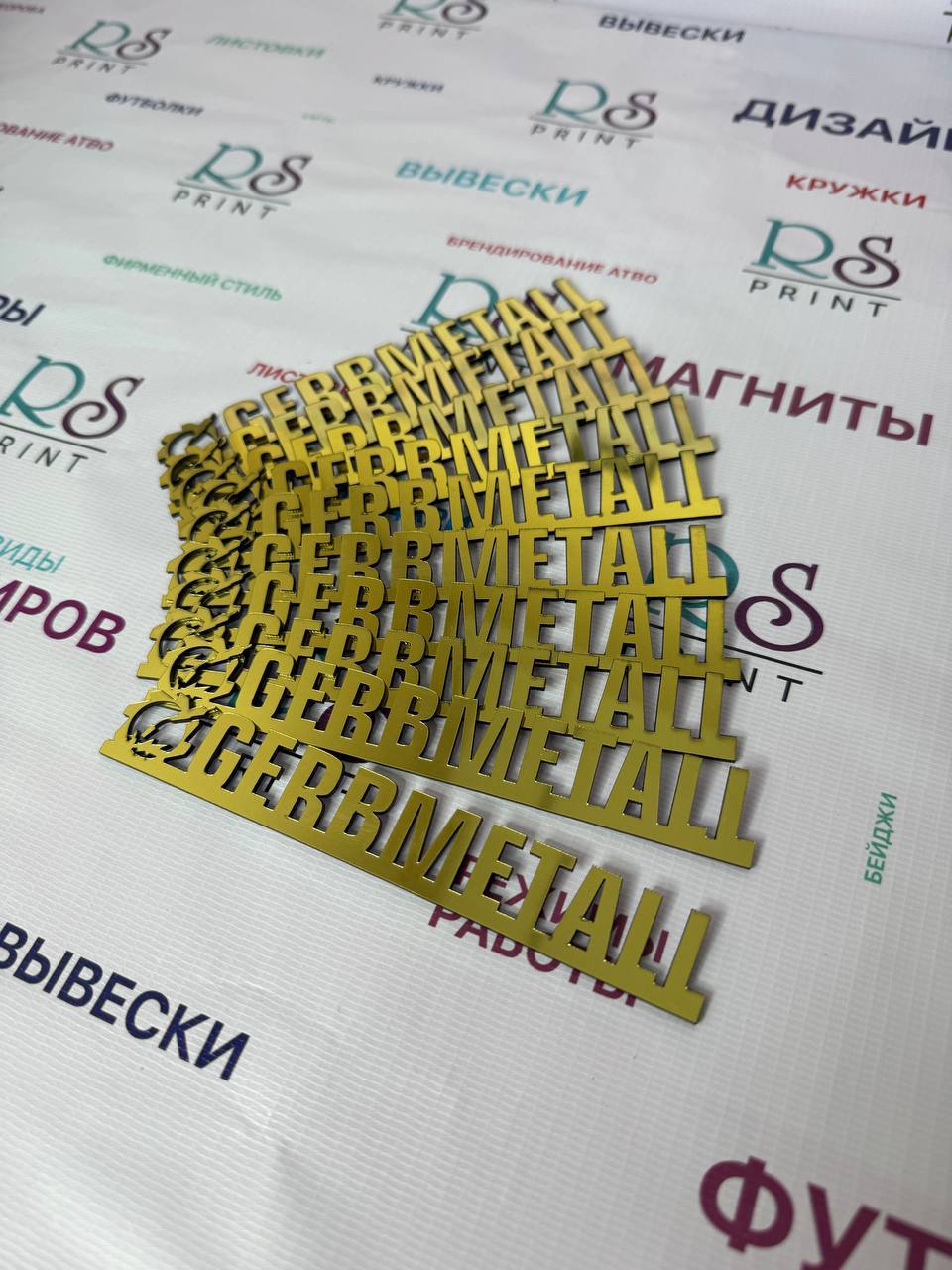 Золотистые буквы GEBBMETALL, вырезанные лазером, стопкой на столе